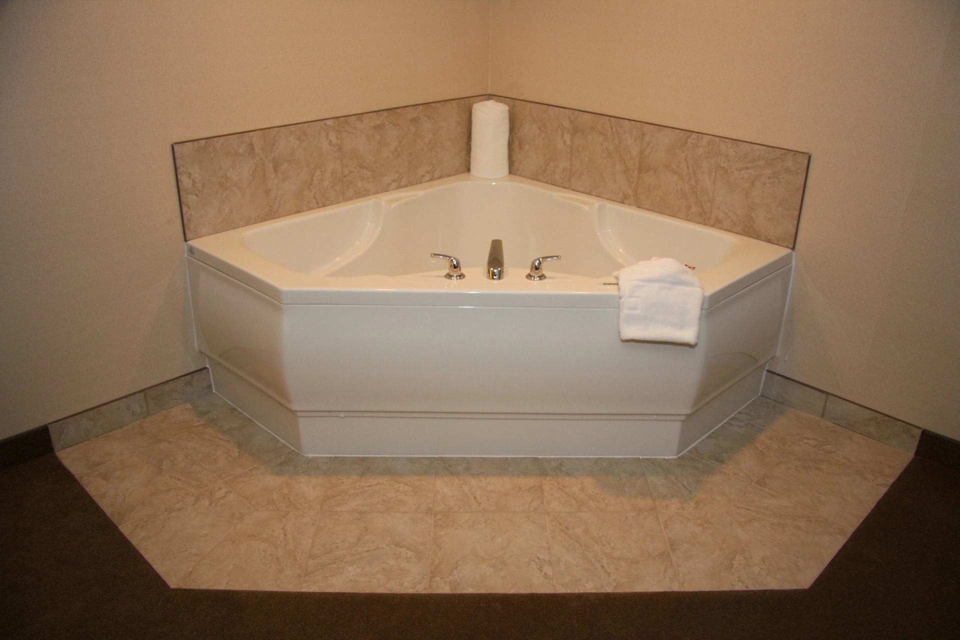 Corner whirlpool tub with beige tile surround and white towel.