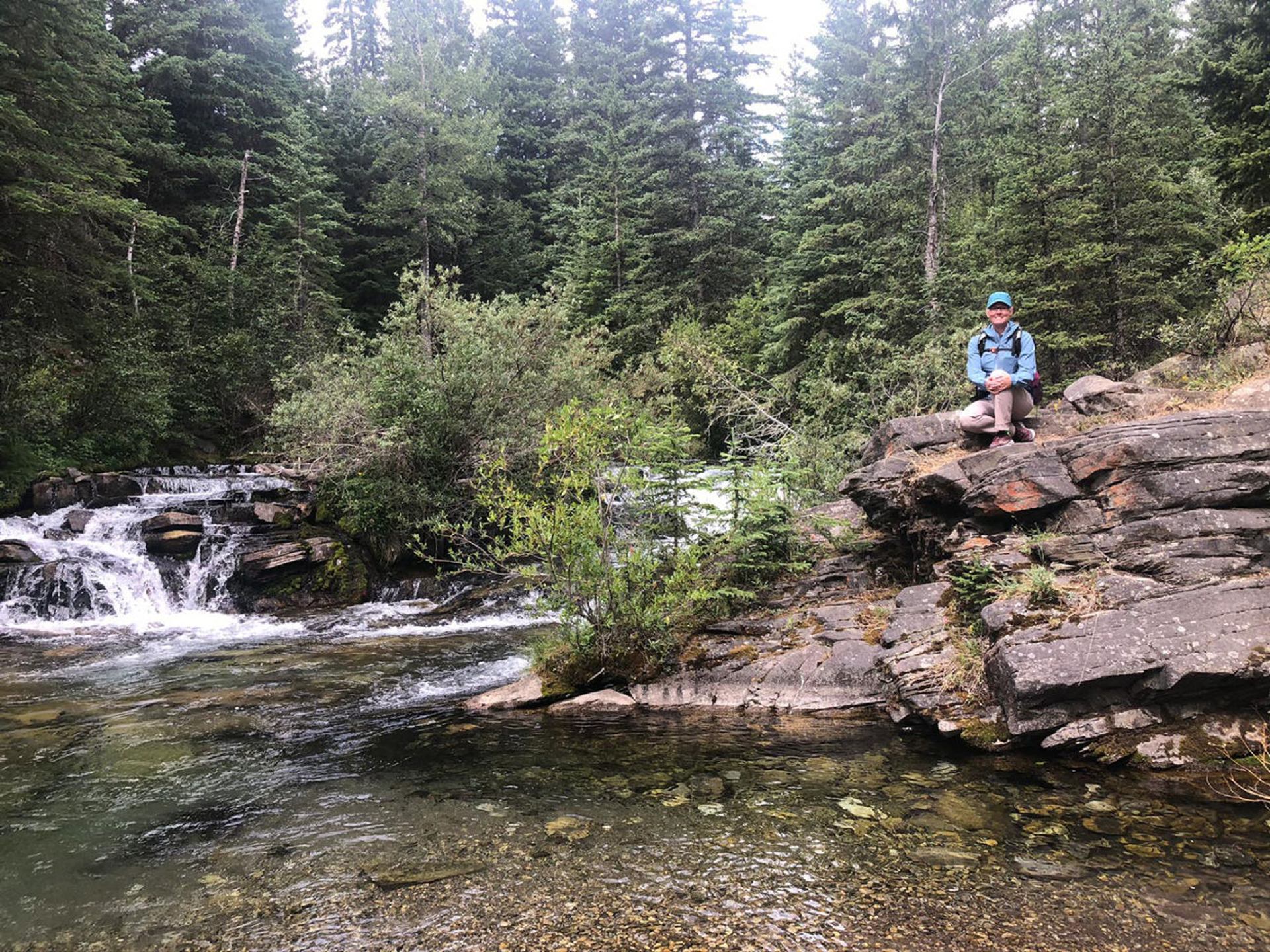 Person sitting on a rock overlooking a small waterfall and creek.