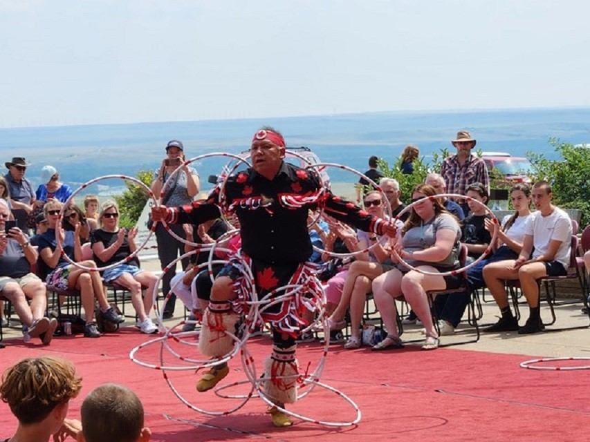 Performer in hoop dance on red carpet with audience and water view.