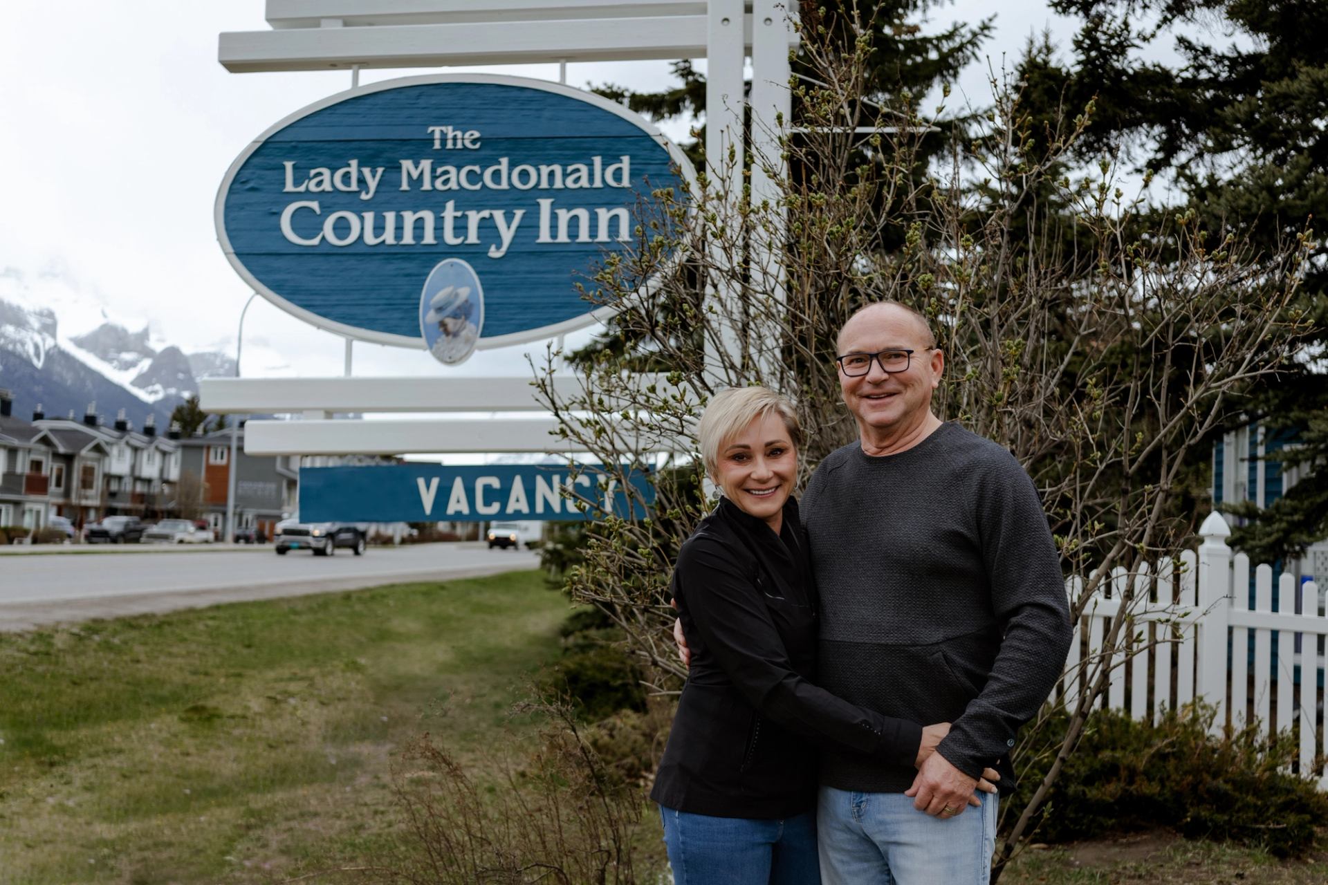 The Lady Macdonald Country Inn sign behind a couple standing outdoors near a driveway.