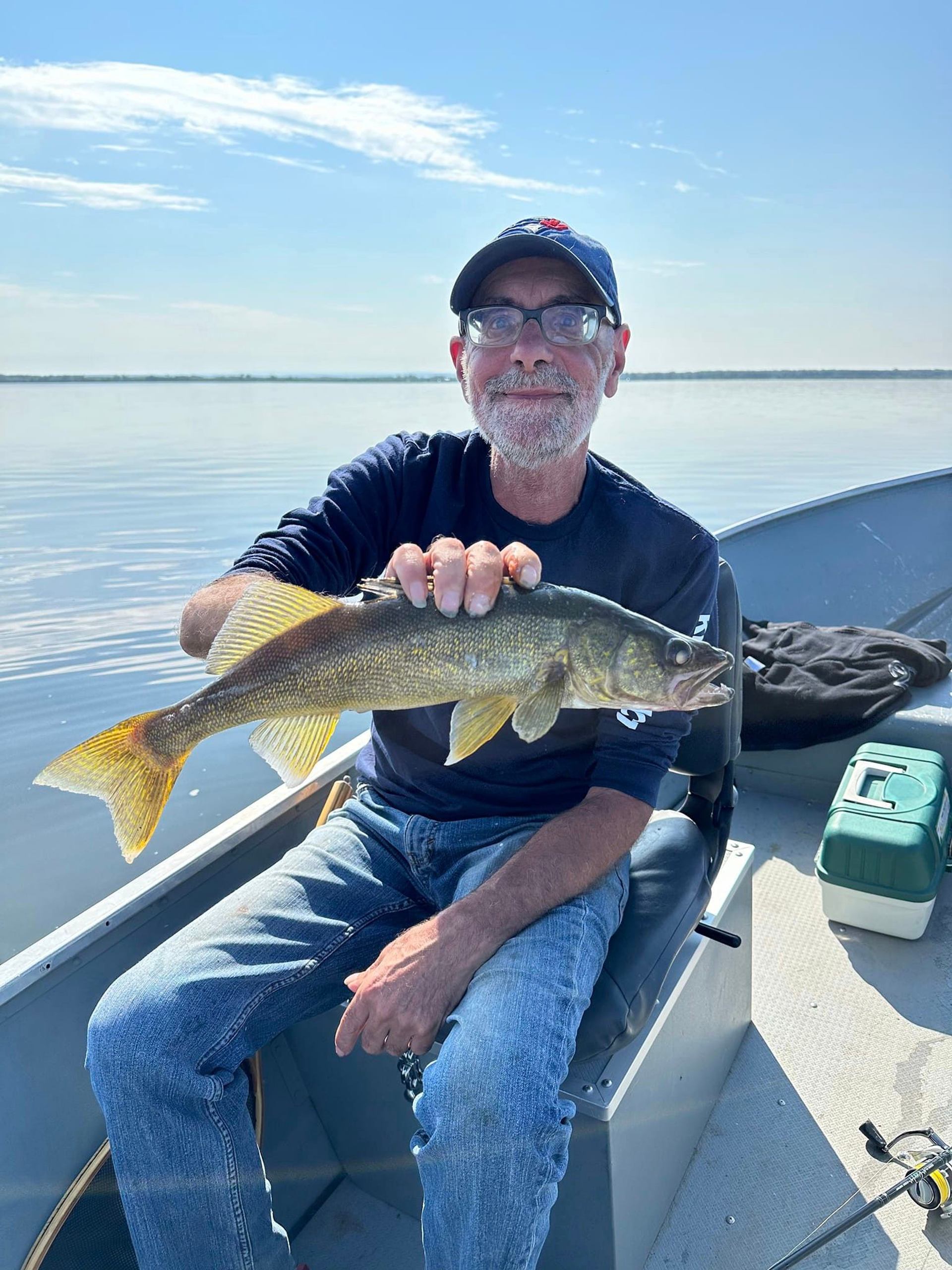 Person wearing glasses and a cap holds a large fish aboard a boat.