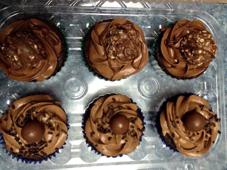 Chocolate cupcakes with swirled frosting in clear plastic clamshell container.
