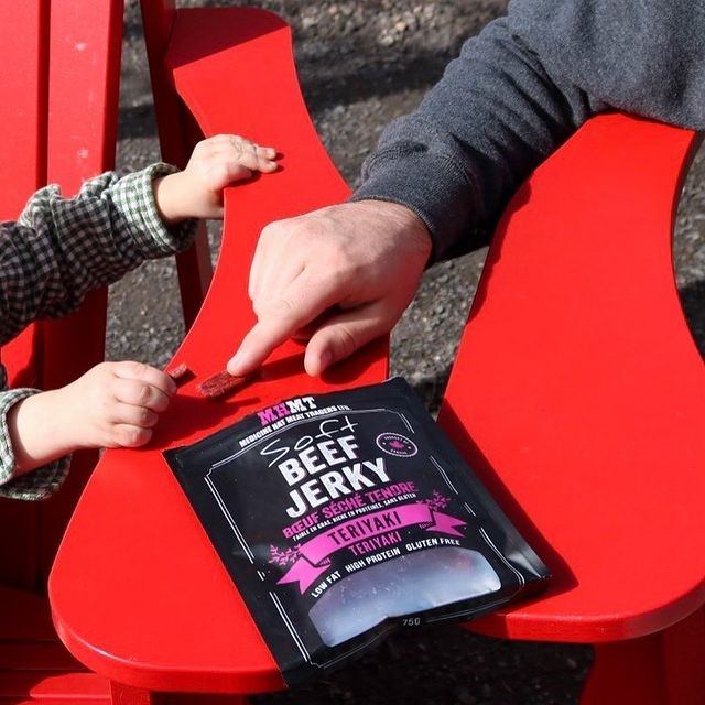 Adult and child sharing beef jerky on red chairs outdoors
