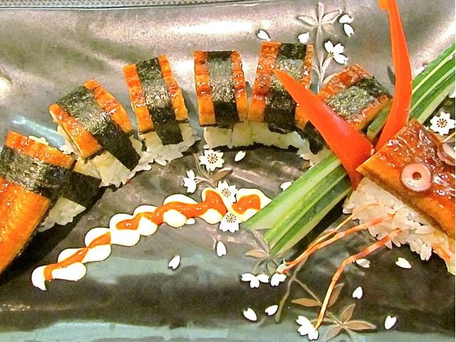 Decorative sushi roll arranged like a dragon with eel, rice, seaweed, and vegetable garnishes.