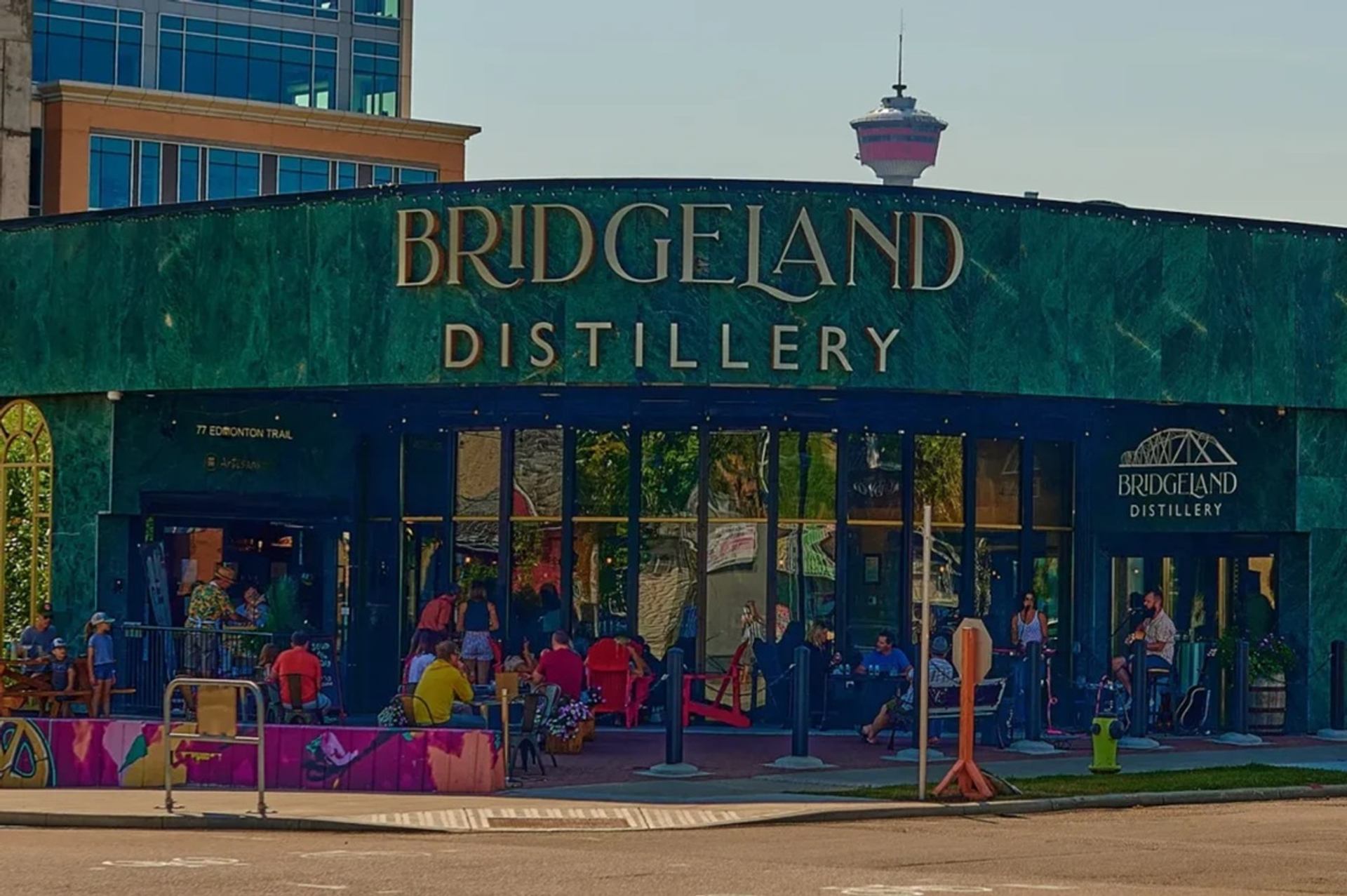 Bridgeland Distillery exterior with green facade, patio seating and people gathered outside.