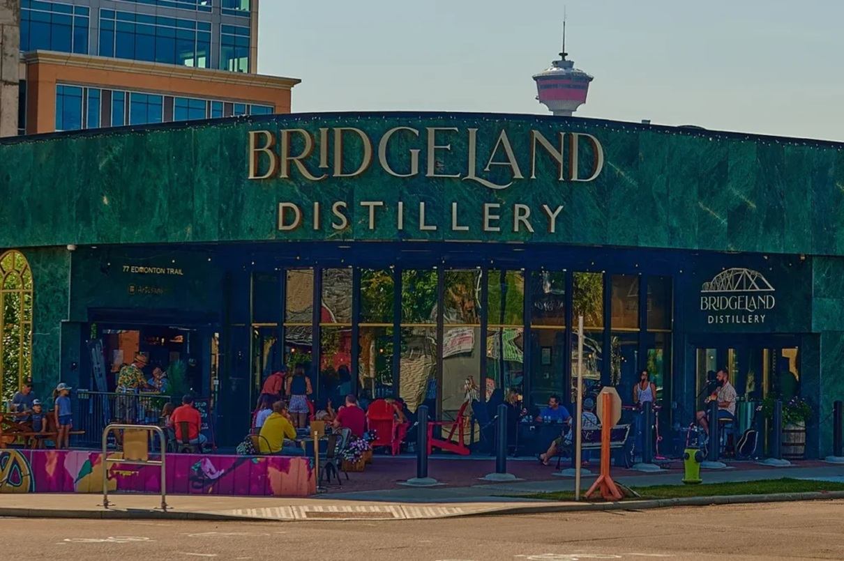 Bridgeland Distillery exterior with green facade, patio seating and people gathered outside.