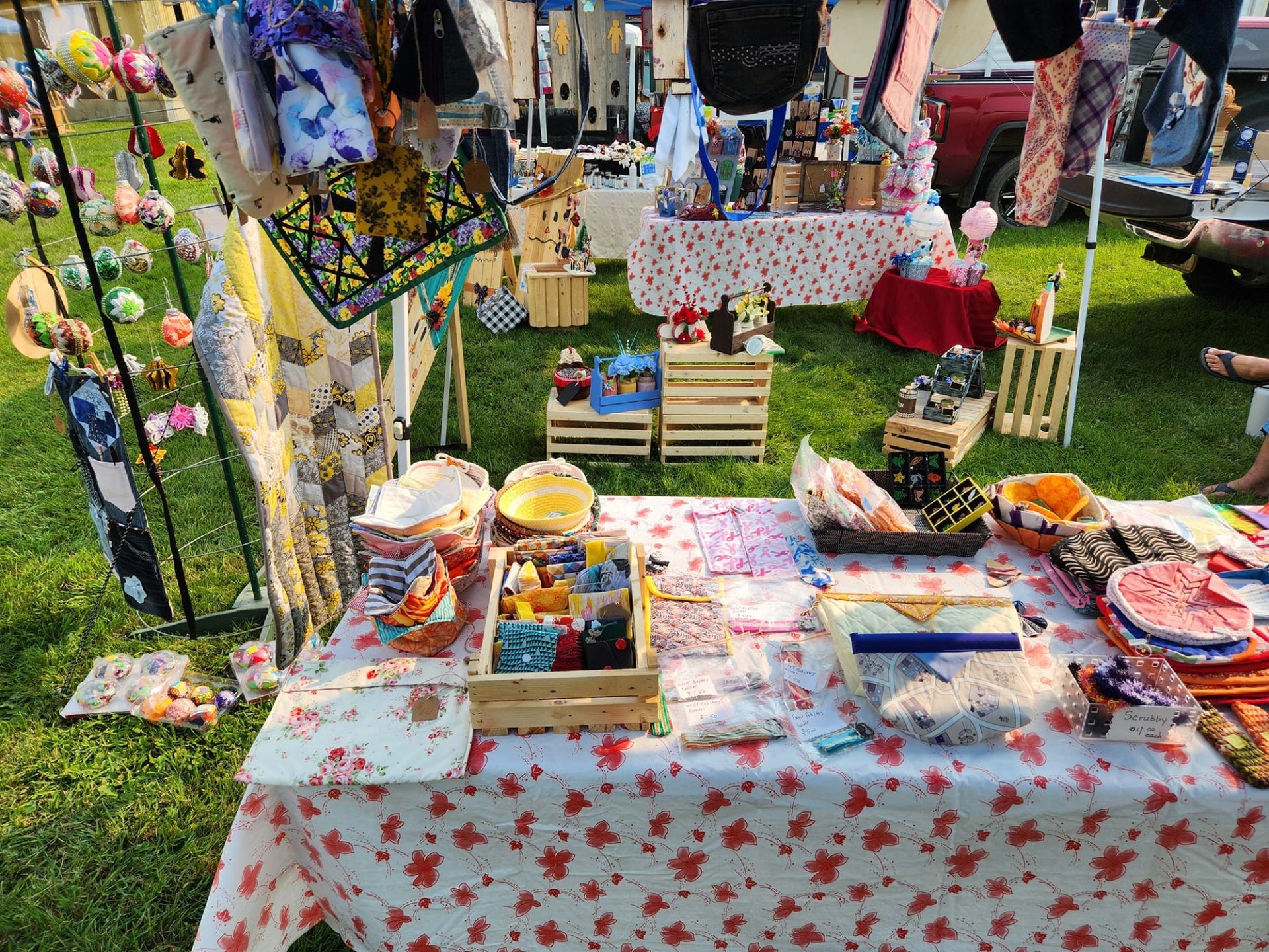 Vendor displays handcrafted quilts, sewn goods, ornaments, bags, and artisan gifts at Kinuso Farmers' Market.