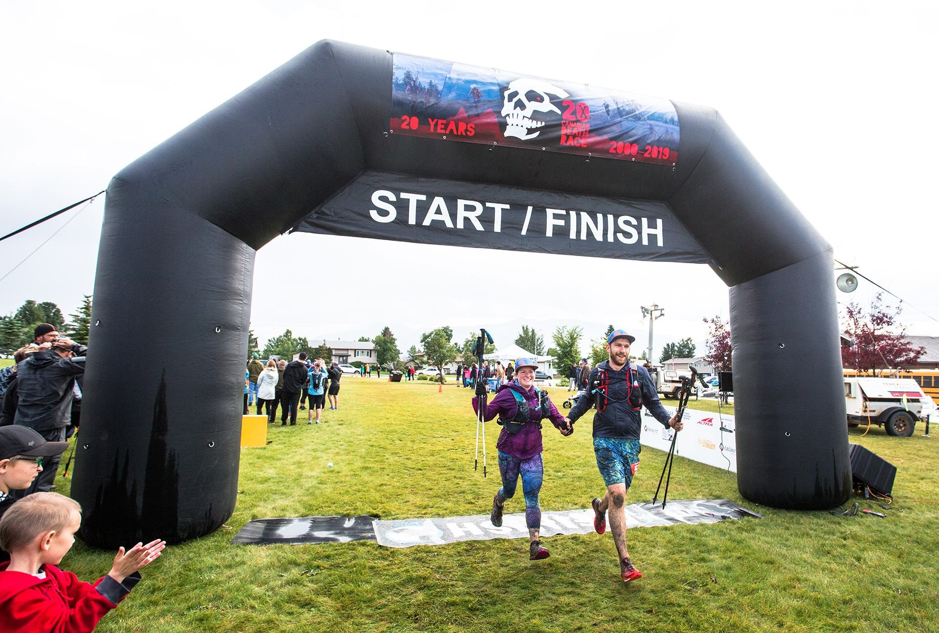 Runners cross the Canadian Death Race start/finish arch on a grassy field.