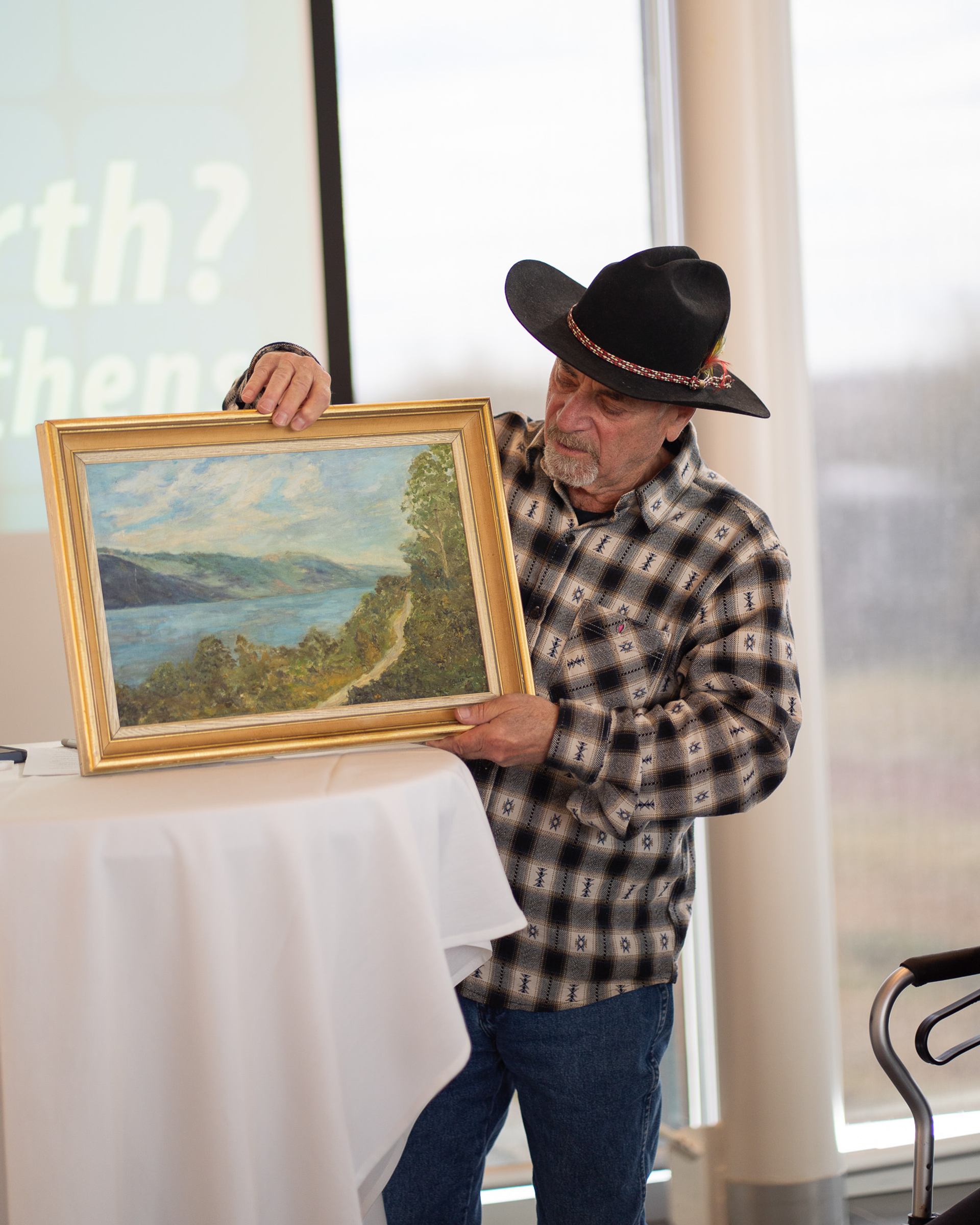 Person holding a framed landscape painting at an event