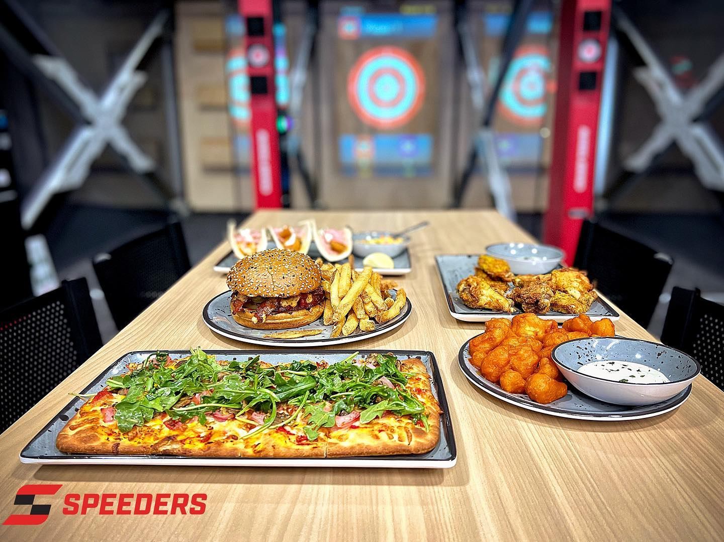 Table with pizza, burger and fries, chicken wings and snacks at Speeders venue.