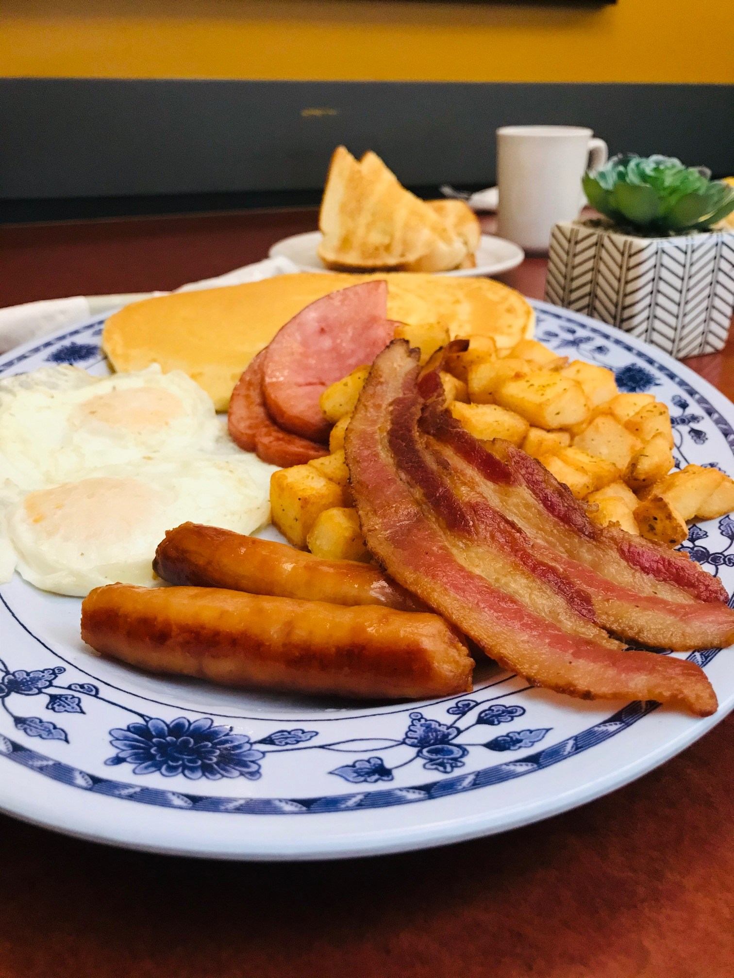 Breakfast plate with bacon, sausage, toast, and fried potatoes, plus a cup of coffee.