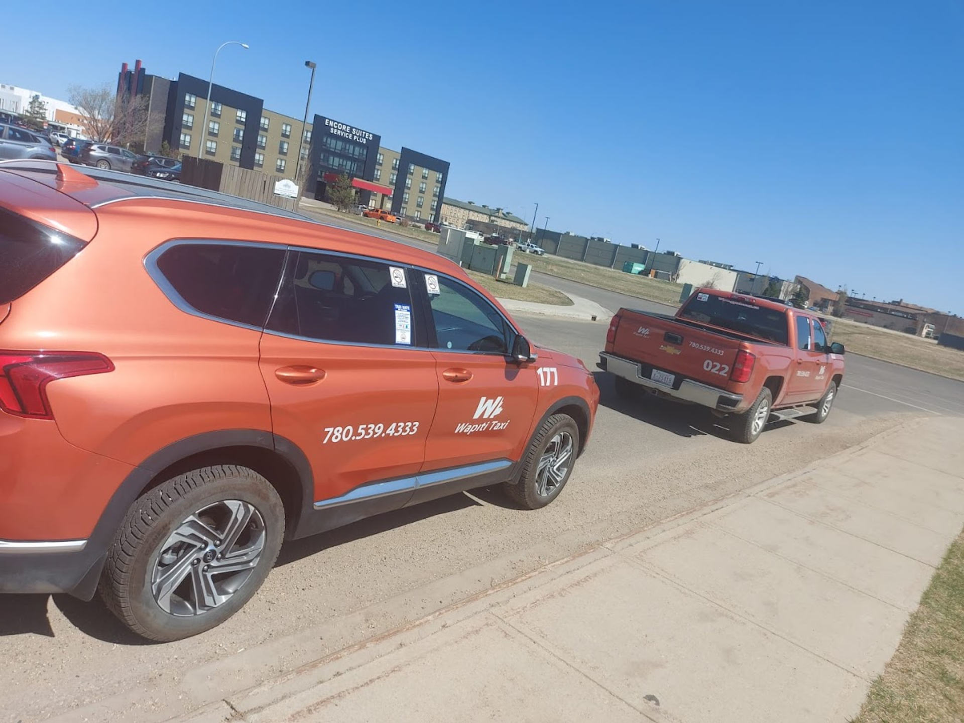 Wapiti Taxi SUV and pickup truck parked beside a sidewalk near Encore Suites.