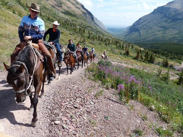 A line of horseback riders travel along a mountainside path.