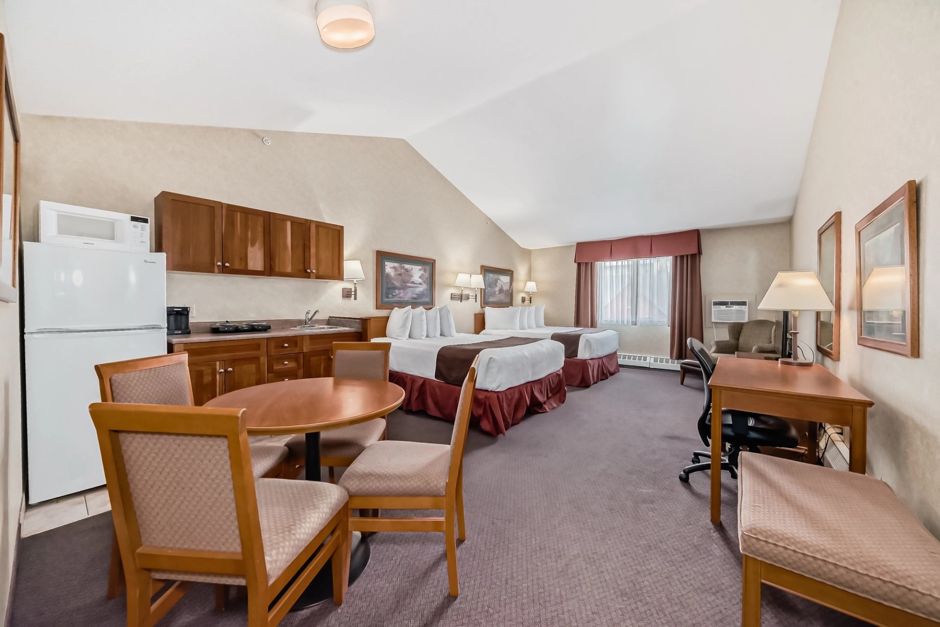 Hotel room with two beds, dining table, and kitchenette including fridge and stove