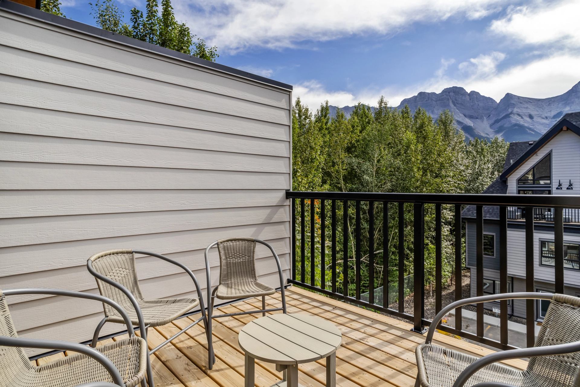 Balcony with wicker chairs and table overlooks trees, neighbouring homes and mountains.