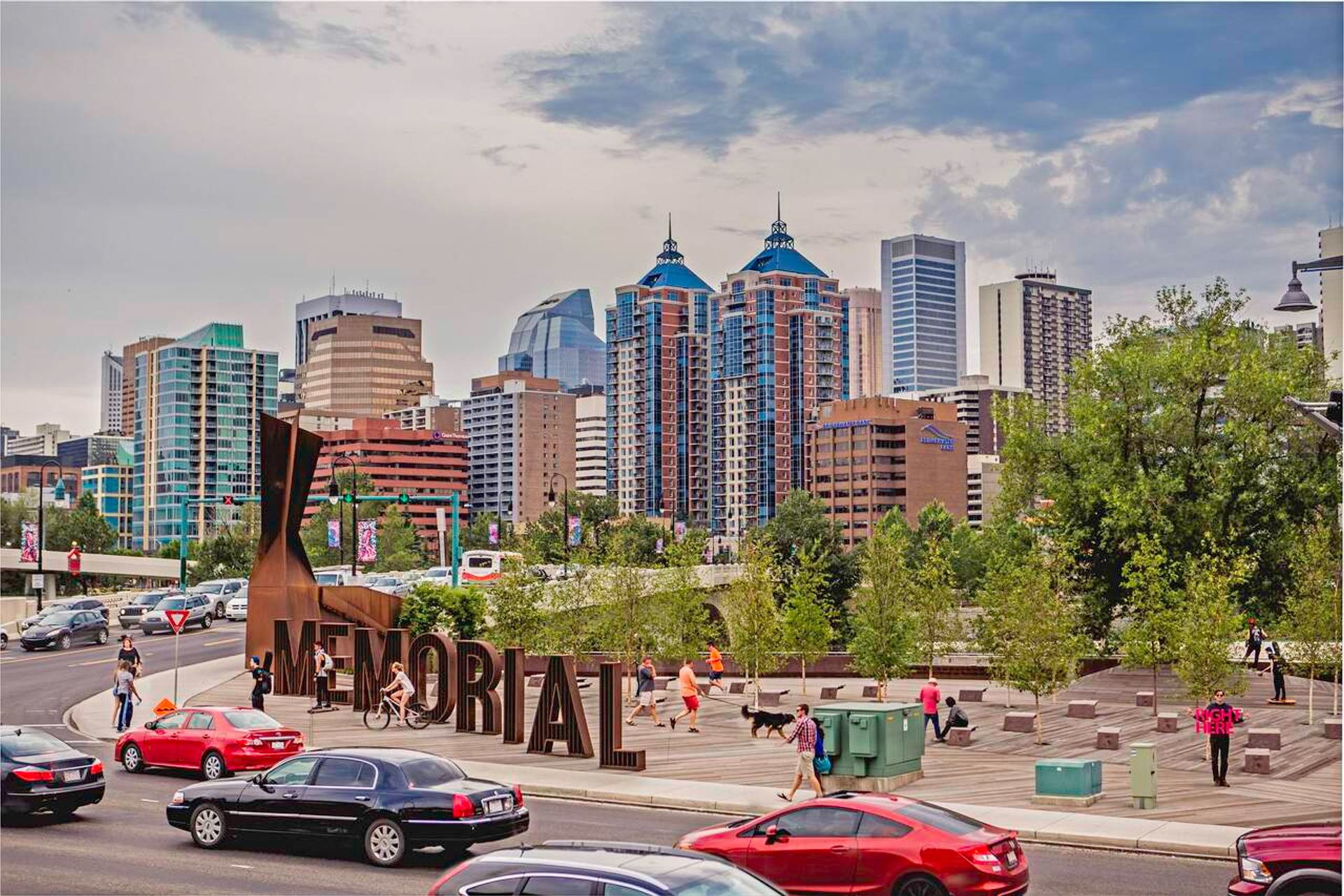 Downtown Calgary skyline behind Memorial Drive park with pedestrians, cyclists and passing traffic.
