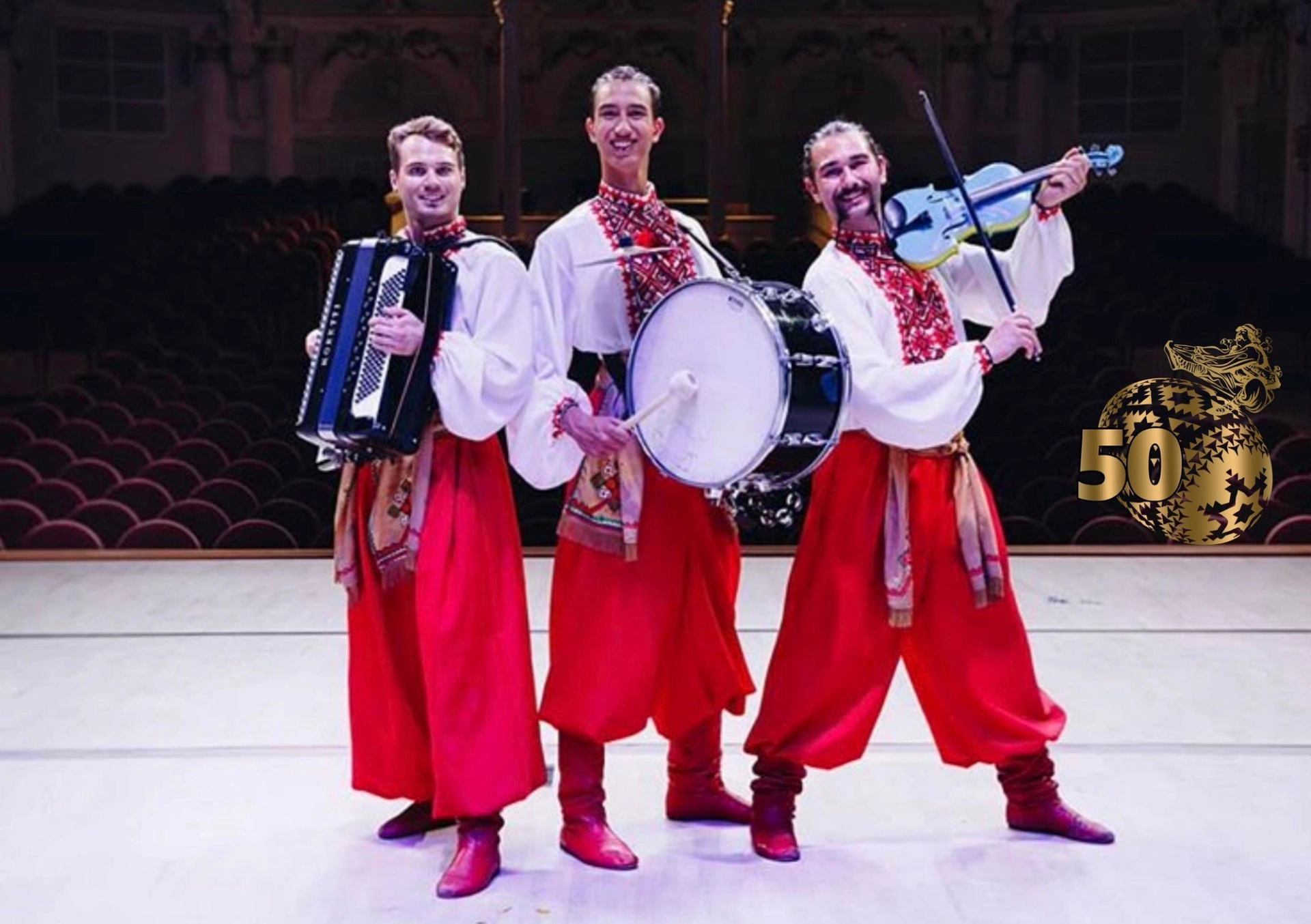 Musicians in traditional dress playing accordion, drum, and violin on stage.