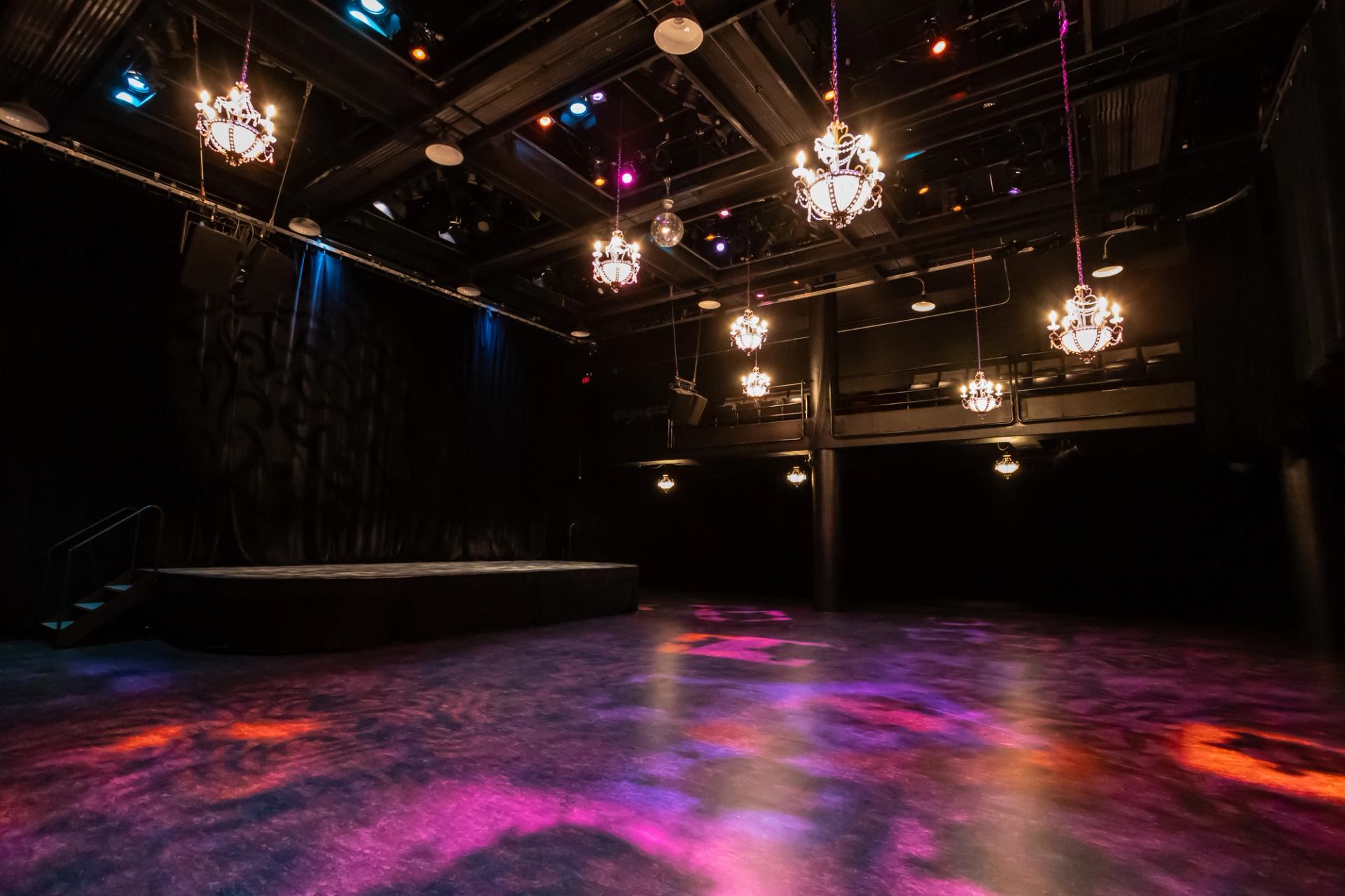 Empty theatre with chandeliers, a raised stage and colourful lights across the floor.