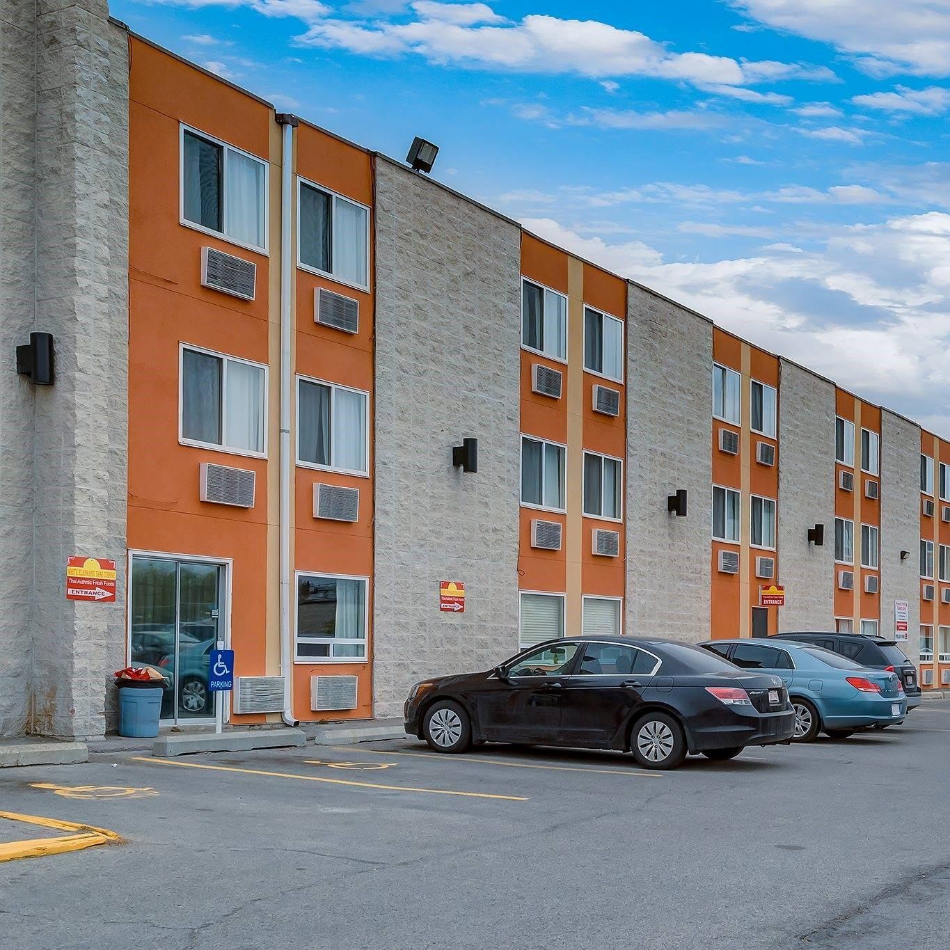 Exterior of Airport Traveller’s Inn with orange accents, multiple windows, and parking lot.