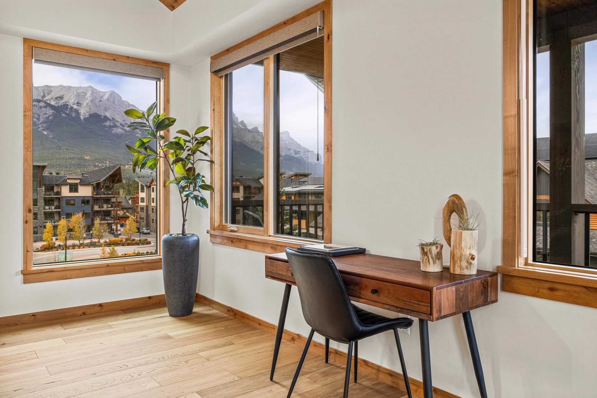 Home office with wooden desk, black chair and windows overlooking mountains.
