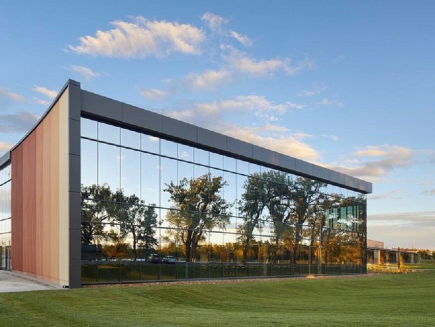 Sleek glass building with reflections, lawn, and a warm cloudy sky.