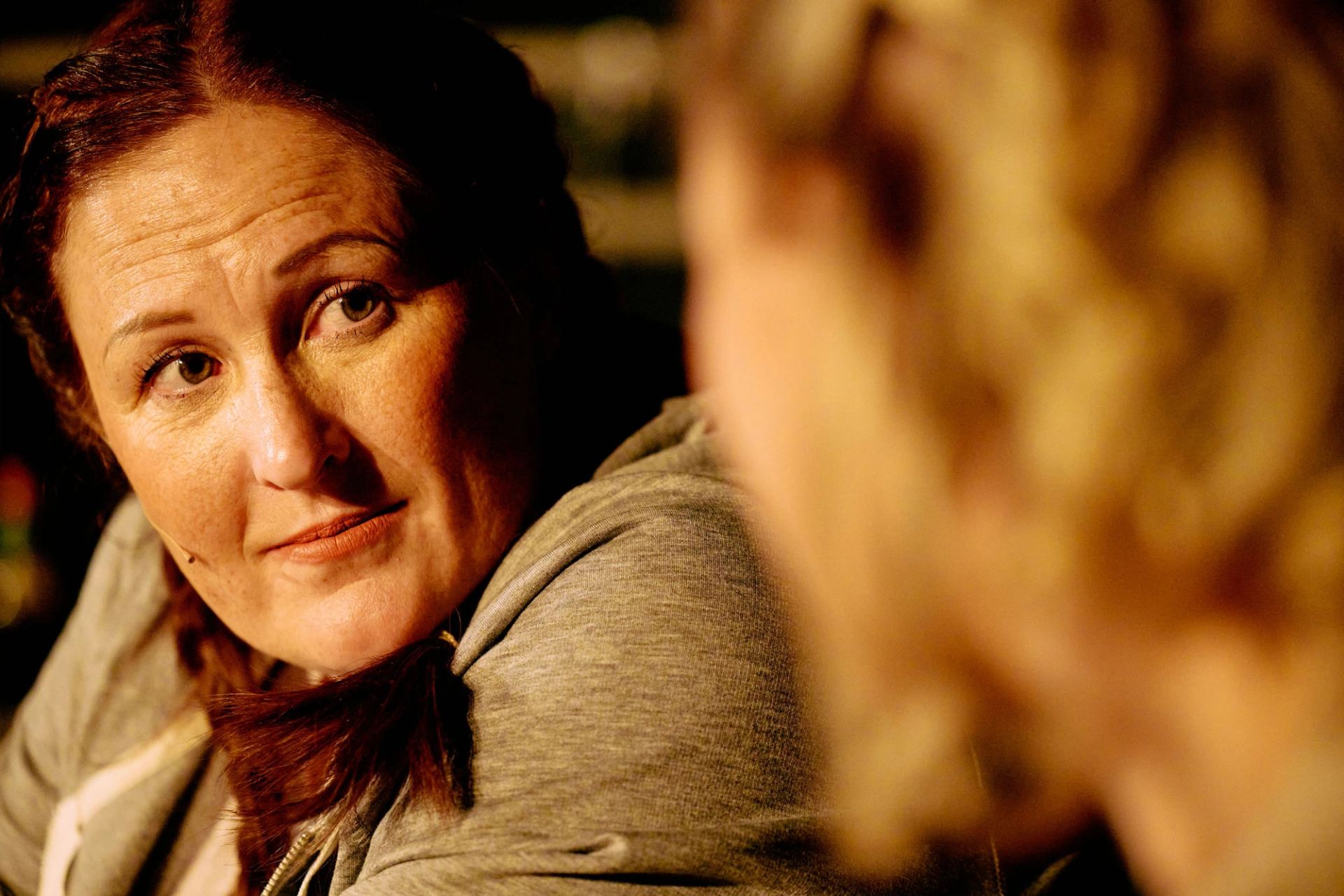 Two people pose closely, woman in close-up and another person beside her in soft focus.