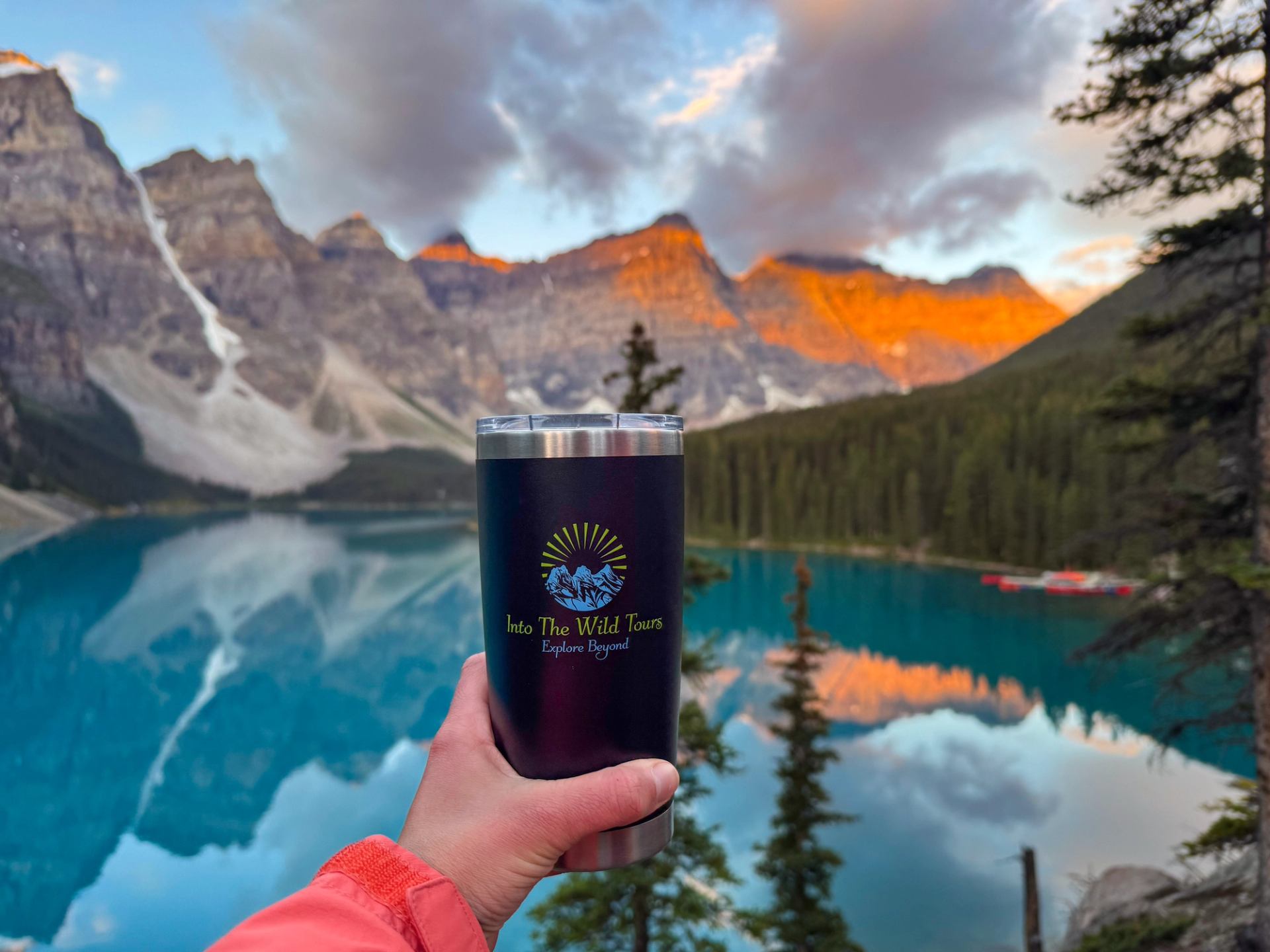 Hand holding tour cup with sunrise lighting Moraine Lake peaks.