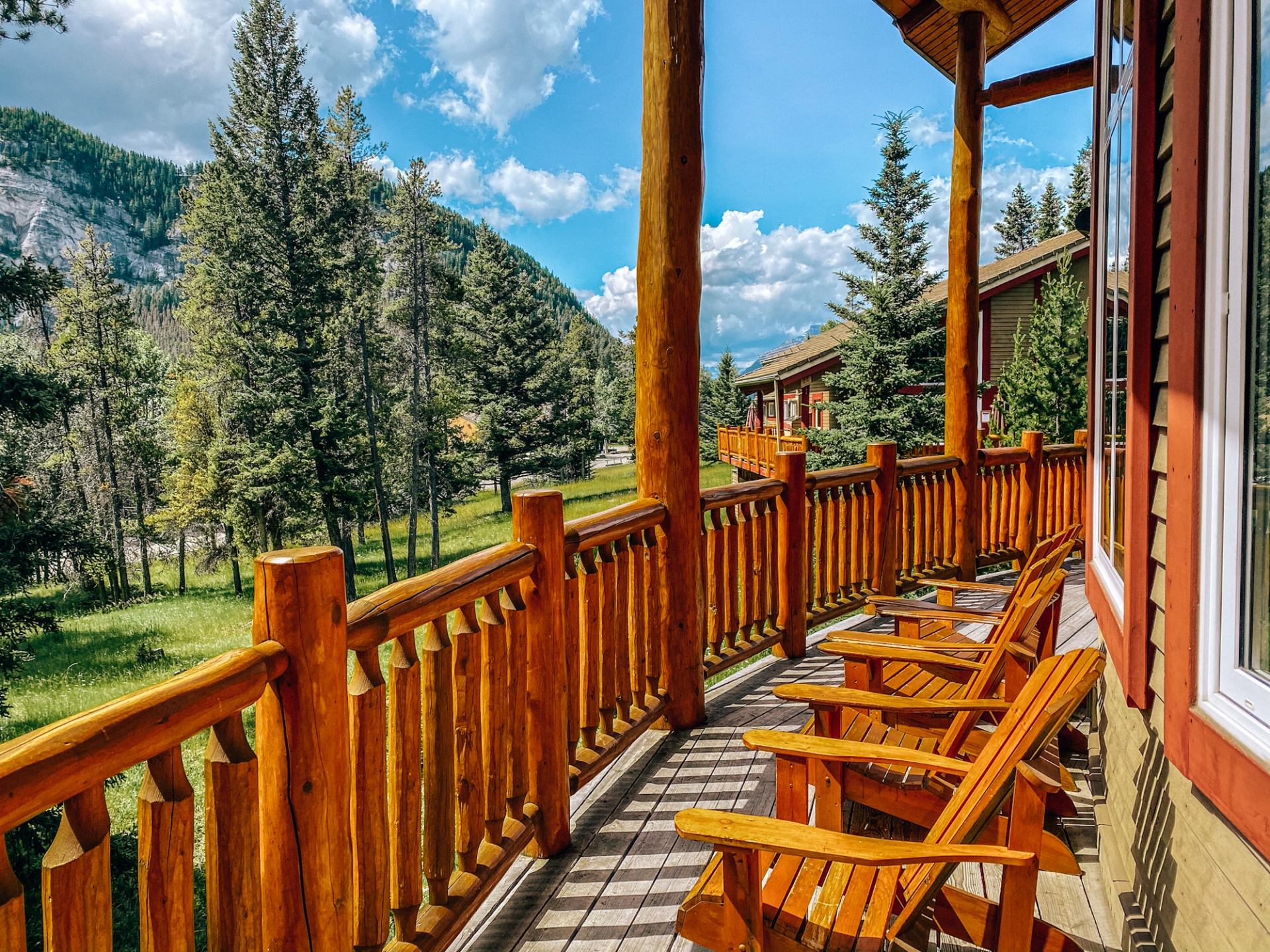Wooden balcony with chairs overlooking pine trees and mountains at HI Banff Alpine Centre.
