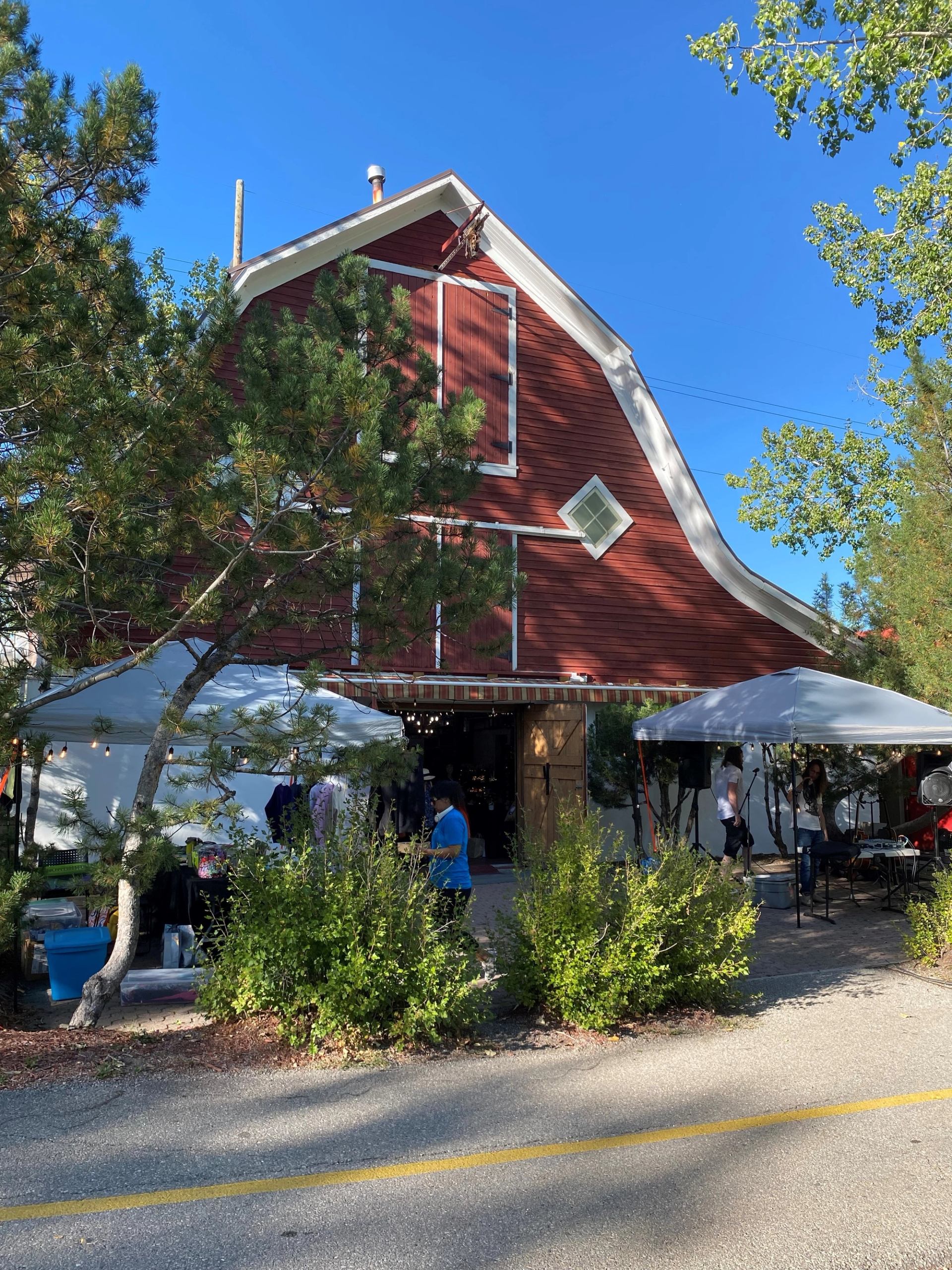 Red barn with tents and vendors outside on a bright, clear market day.