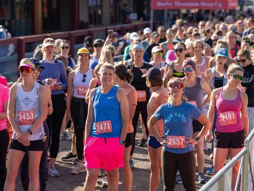 Runners participate in an outdoor race on a street, wearing numbered bibs and sunglasses.