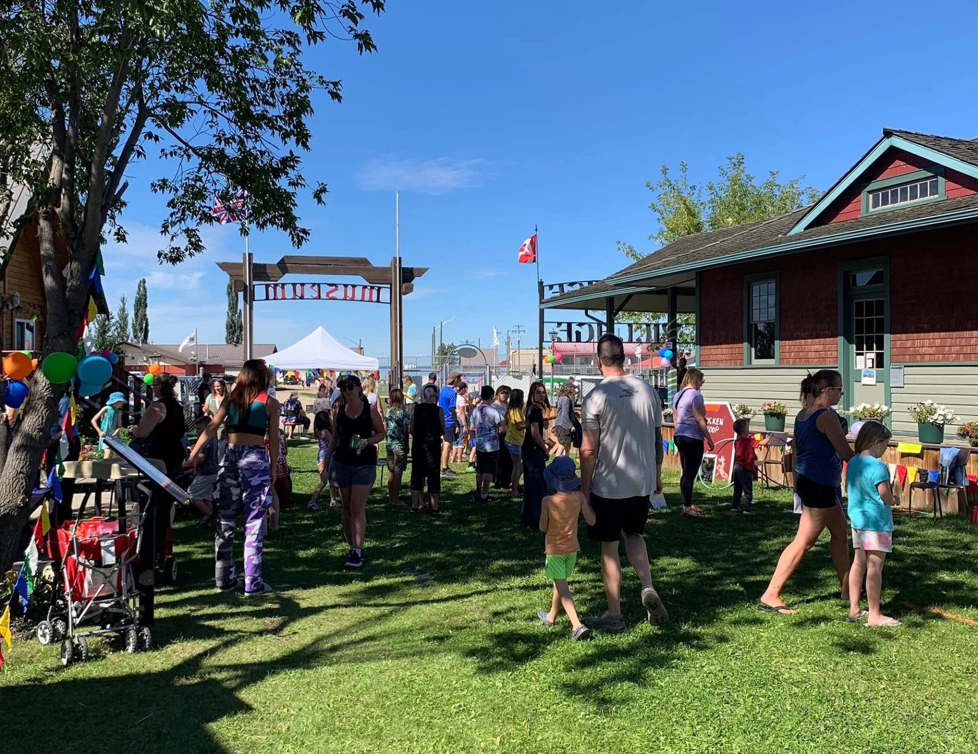 Families gather on grass at carnival with balloons and stroller.
