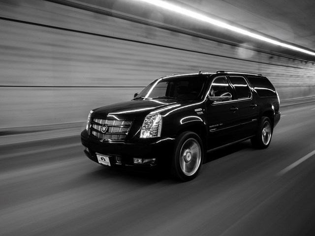 Black Cadillac Escalade by Ambassador Limousine driving through a tunnel with reflections.