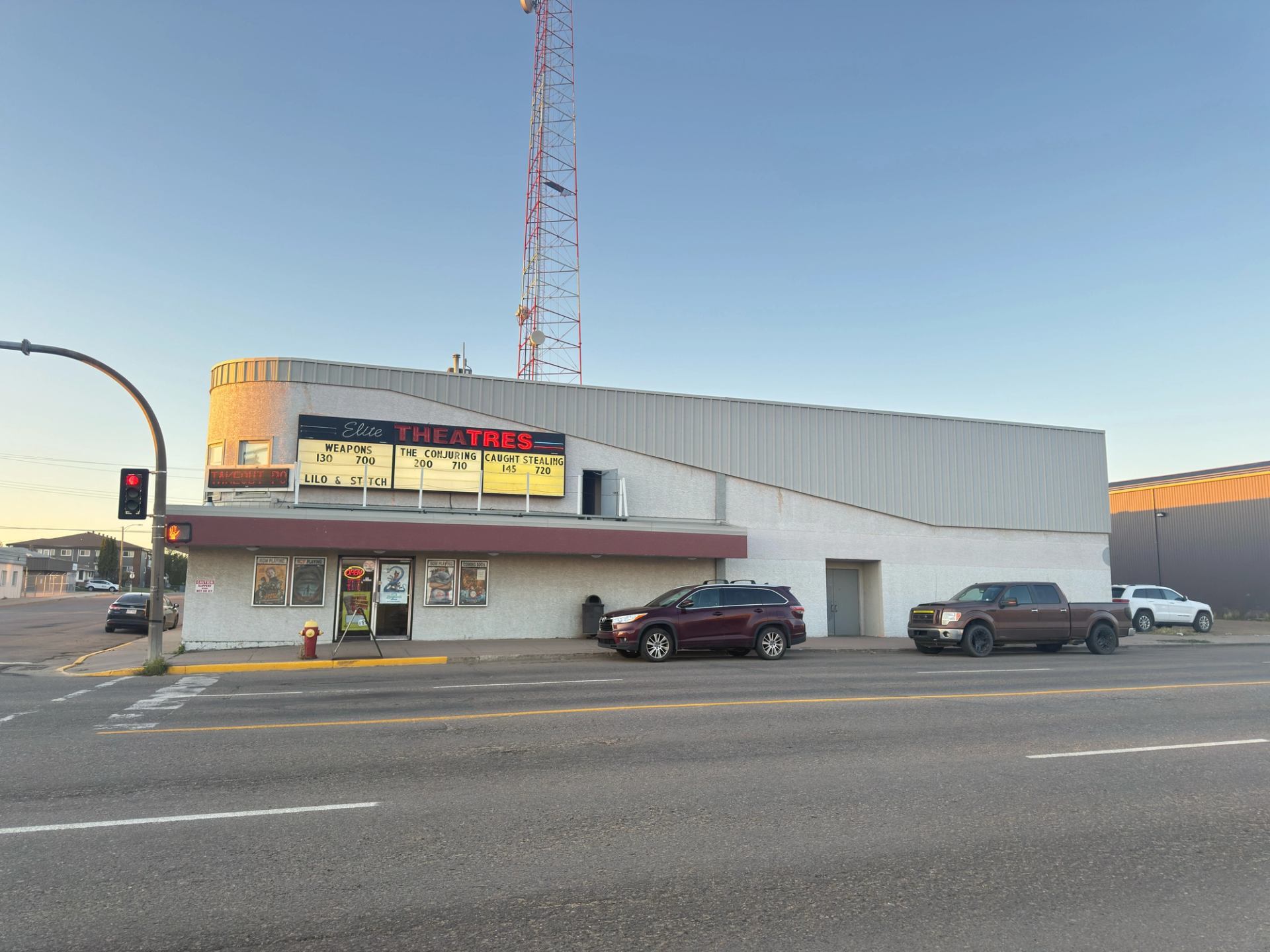 White theatre with marquee, parked cars, and tall antenna.
