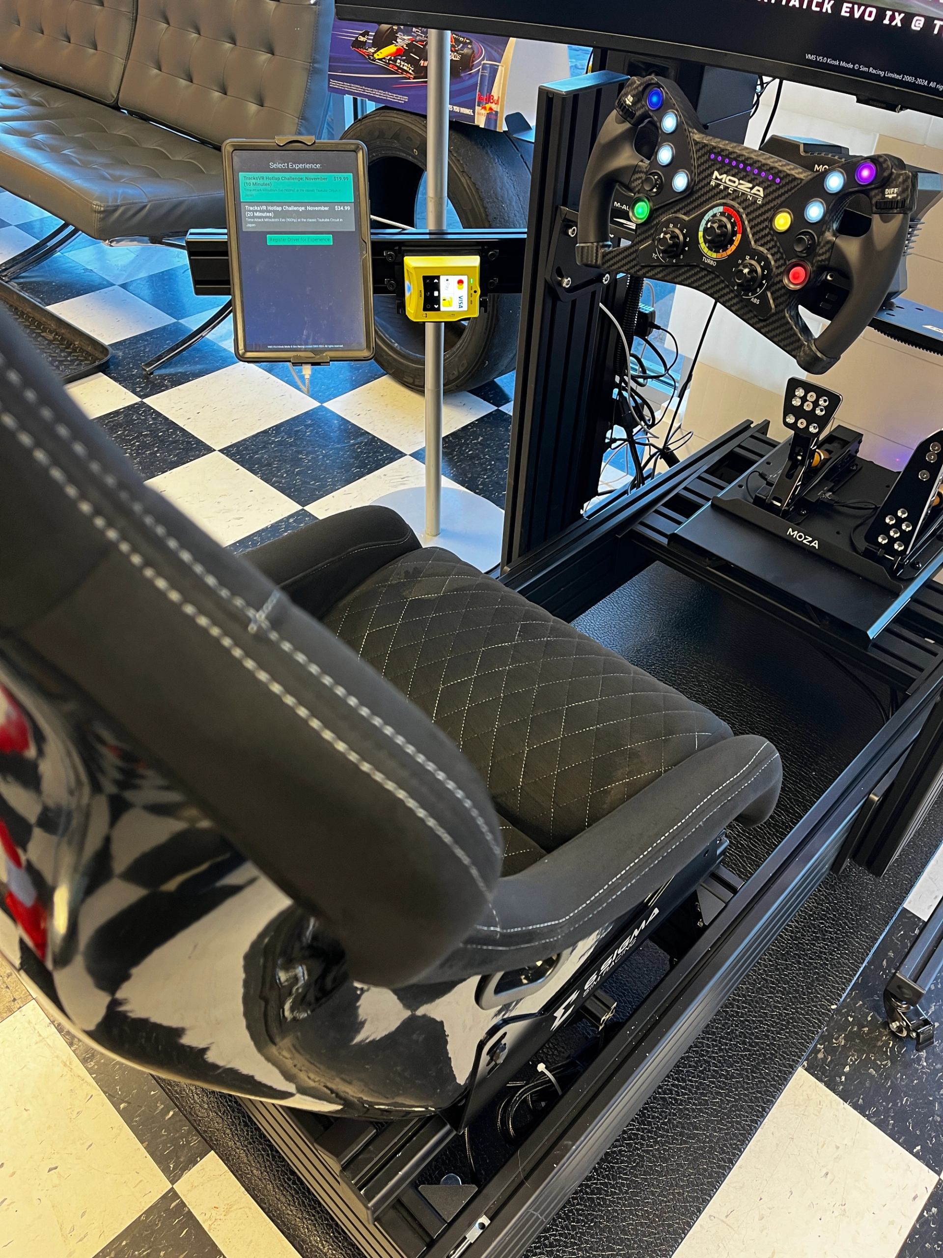 Racing simulator with black seat, steering wheel, and checkered floor.