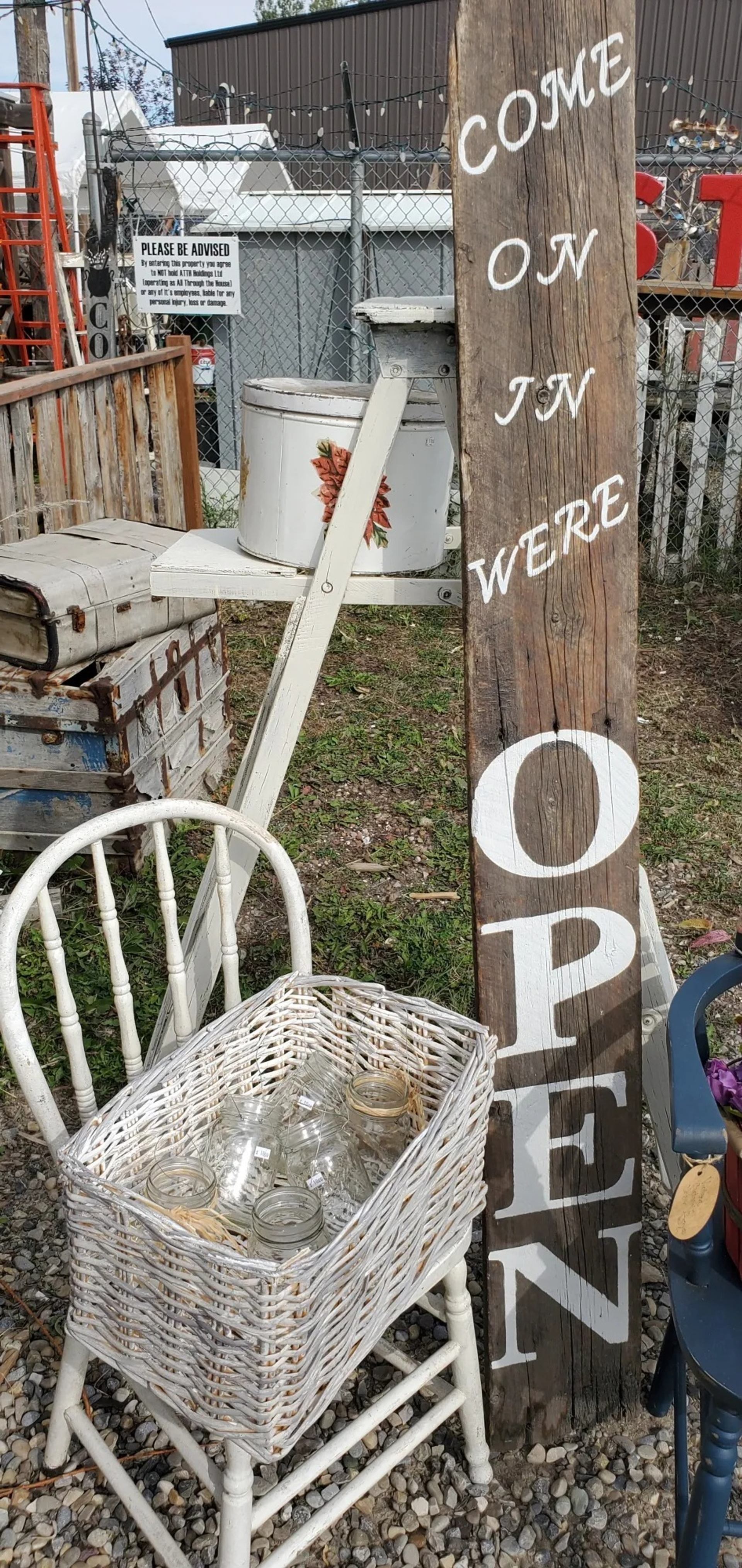 Rustic outdoor display with wooden OPEN sign, wicker basket of jars, vintage items.