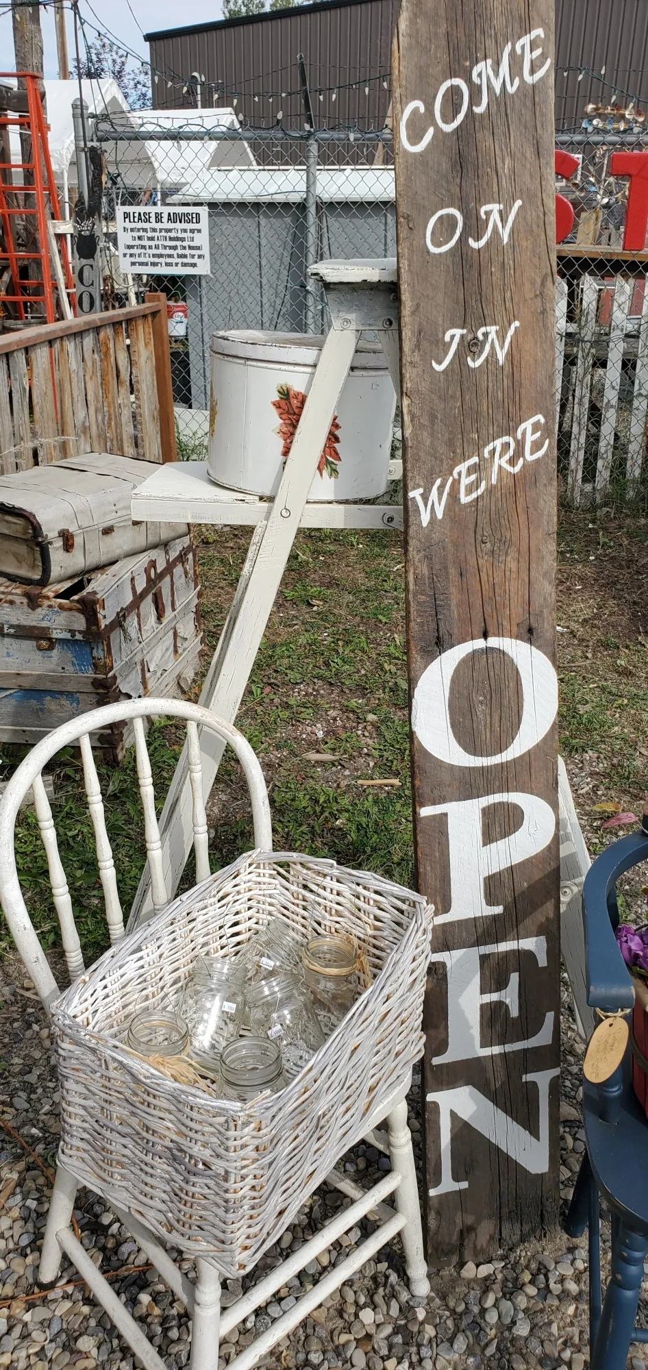 Rustic outdoor display with wooden OPEN sign, wicker basket of jars, vintage items.