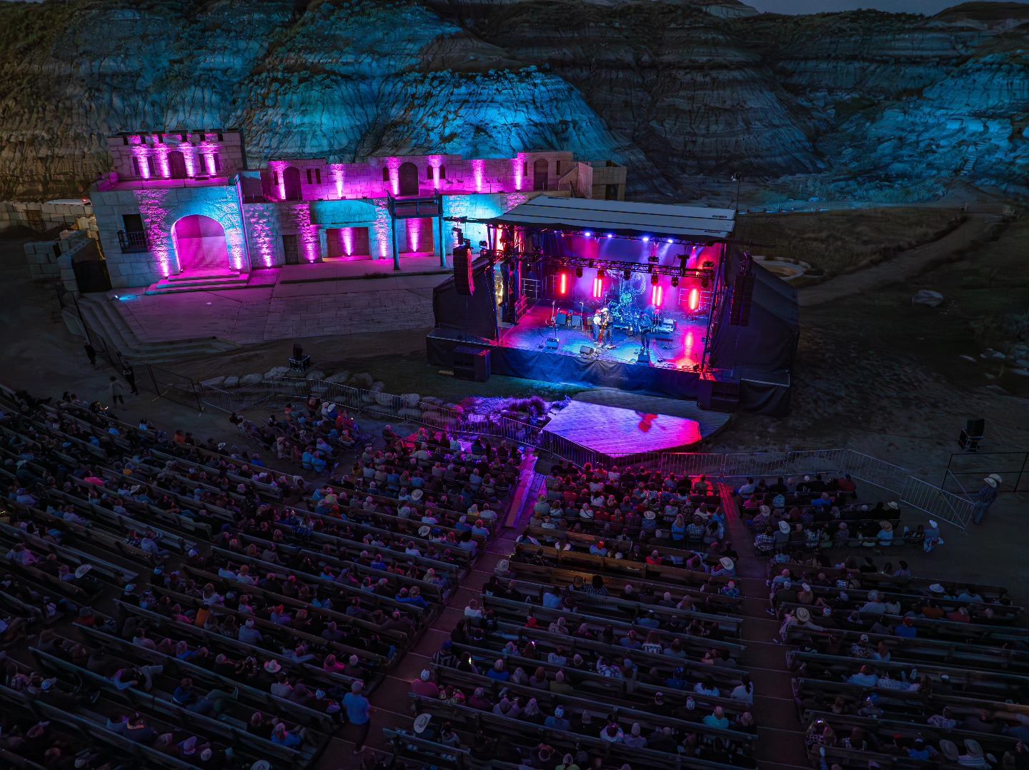 Music festival in Badlands with vibrant lights and seated crowd.