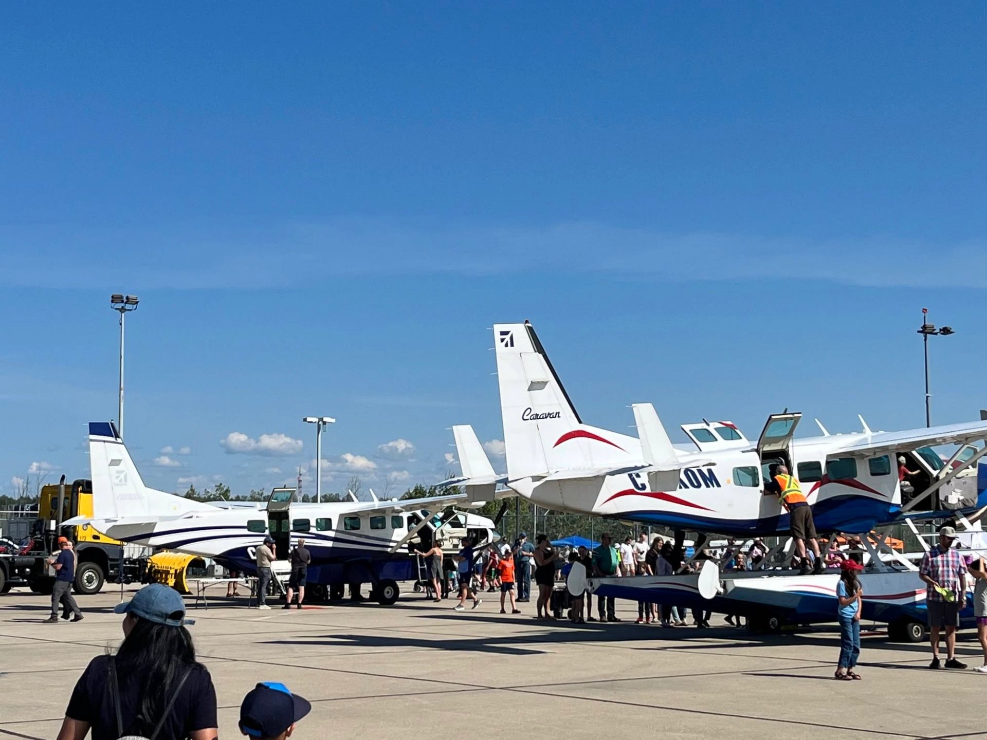 Crowds gather around small aircraft displayed on an airport tarmac.