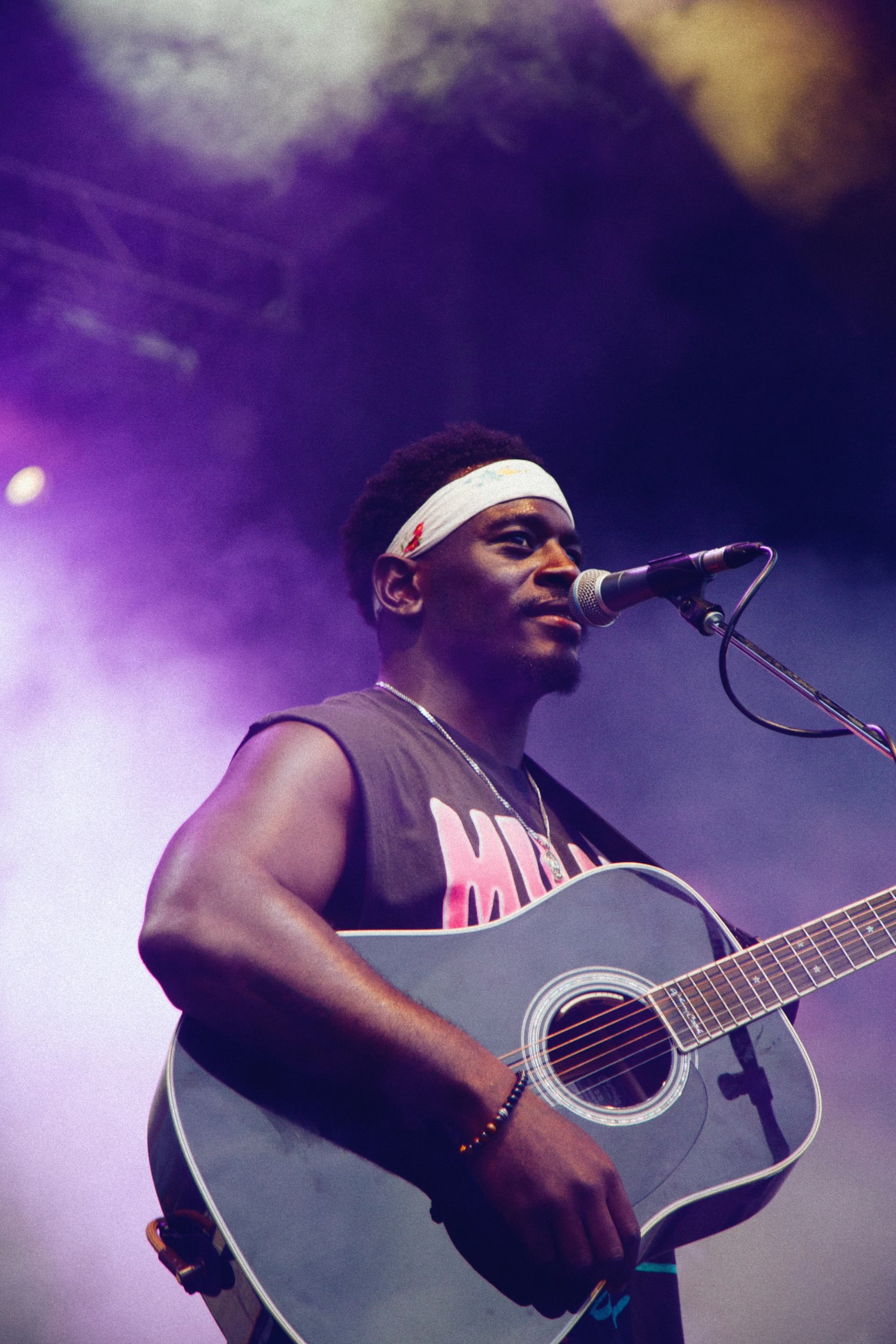Musician playing guitar and singing on a colorful, smoky stage.