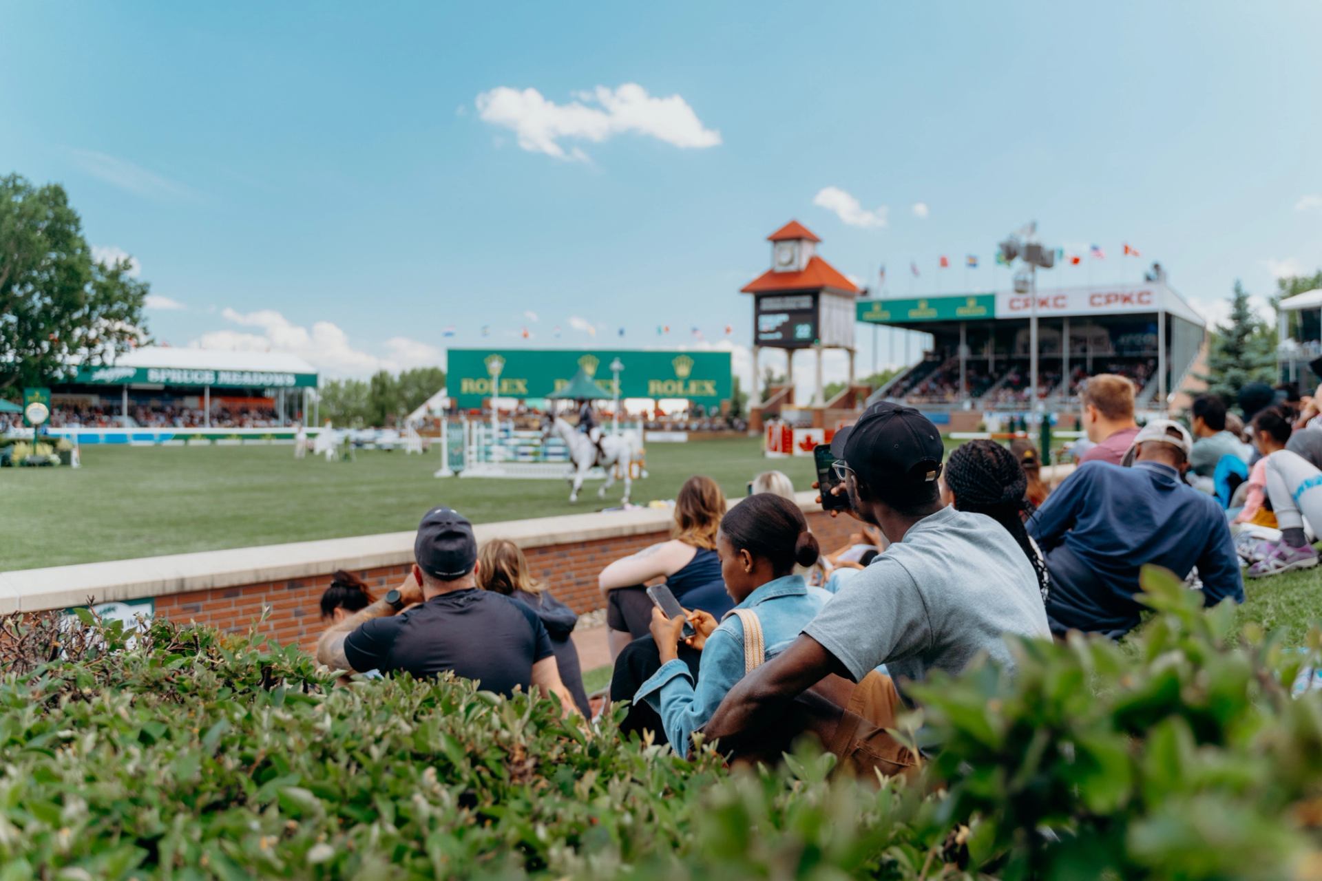 Spectators sit on the grass watching a show jumping round at the National Tournament.