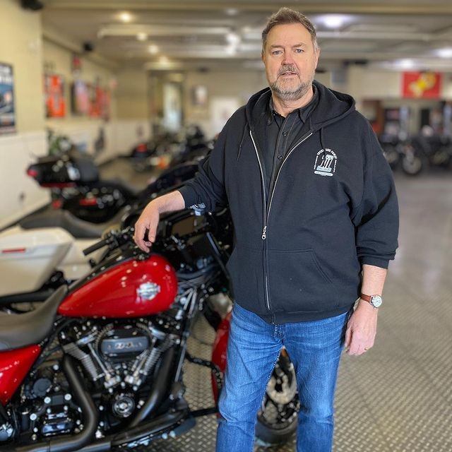 Person in black hoodie stands beside red Harley-Davidson motorcycle inside showroom.