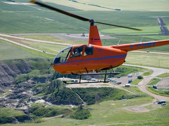 Orange helicopter flying over green fields with roads and buildings below.