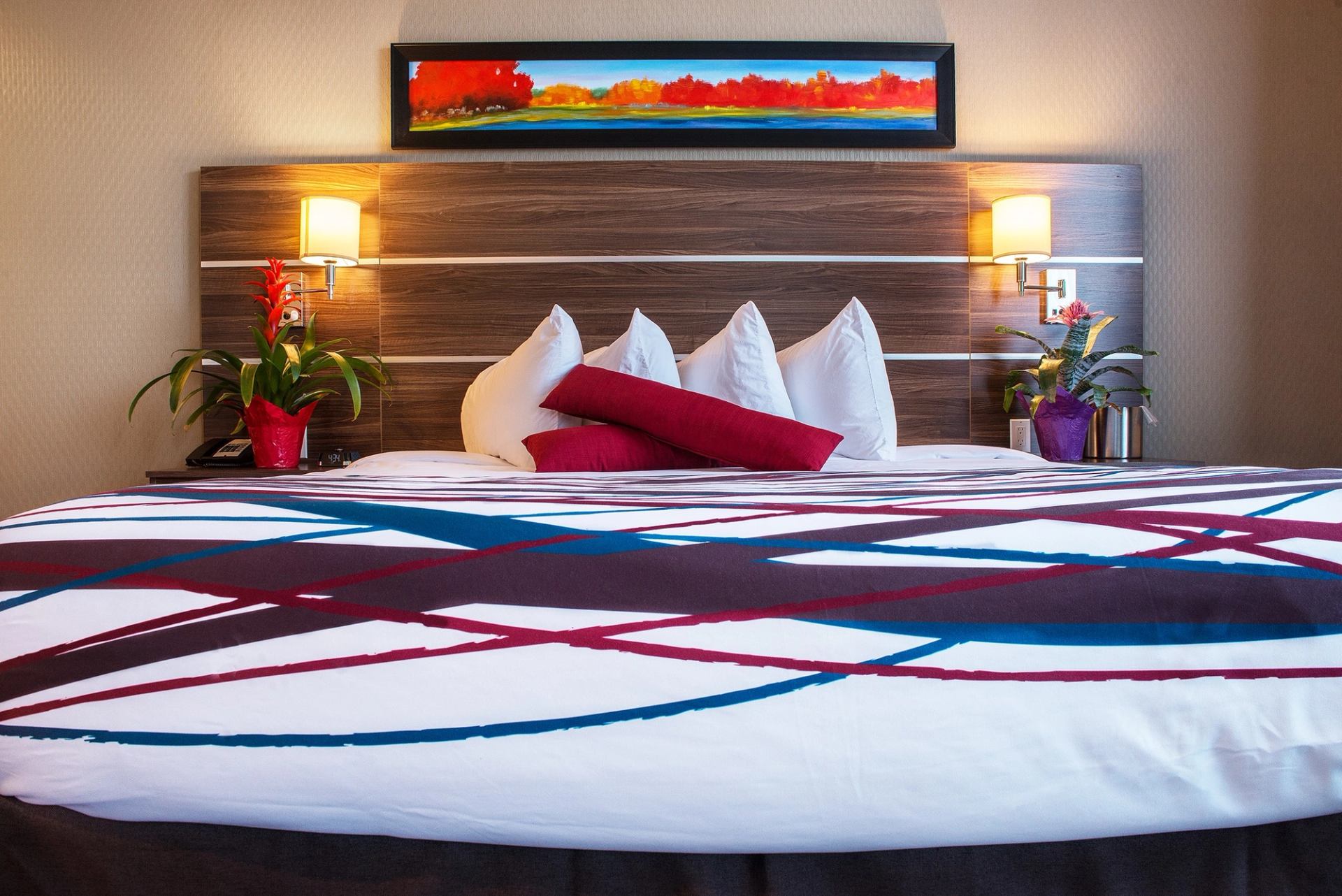 Hotel bed with colorful bedding, pillows, lamps, and artwork above the headboard.