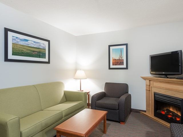 Hotel-style sitting area with green sofa, armchair, TV and electric fireplace.