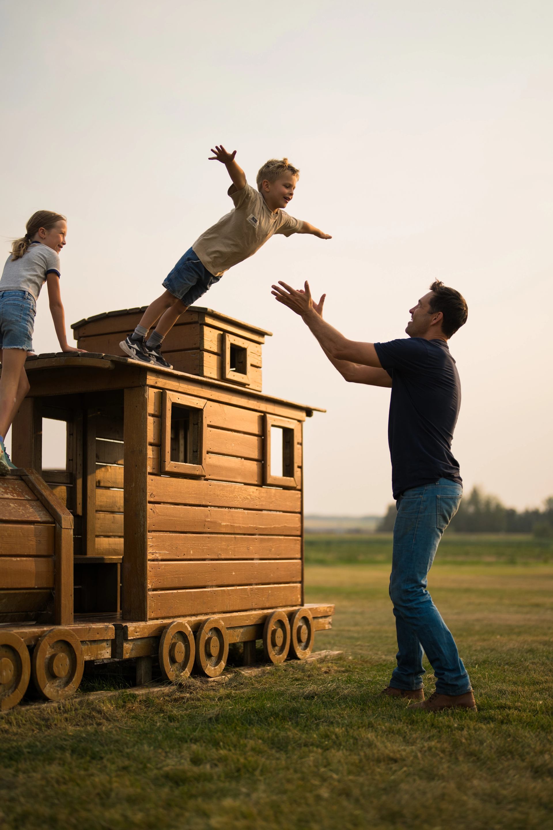 Child jumps from wooden playhouse into adult's arms at The Jungle Farm.