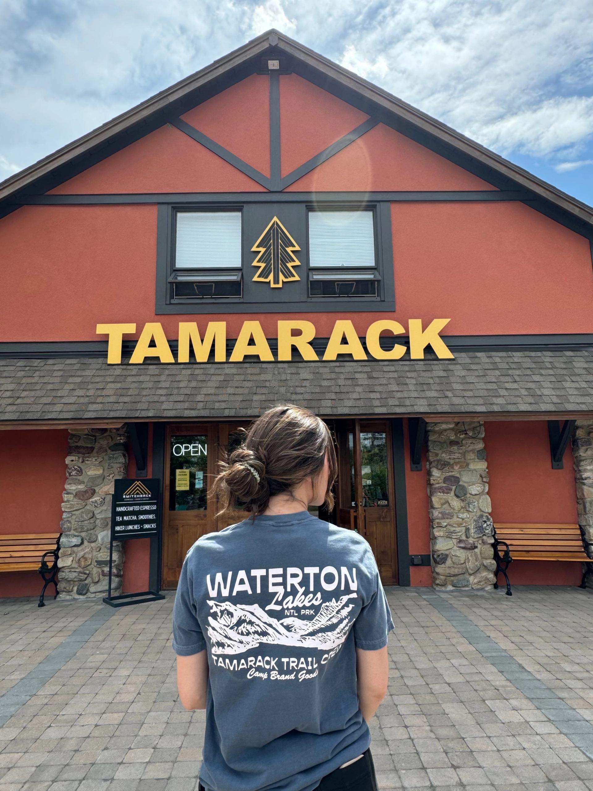 Person wearing a Waterton-branded Tamarack shirt standing in front of the Tamarack building entrance.