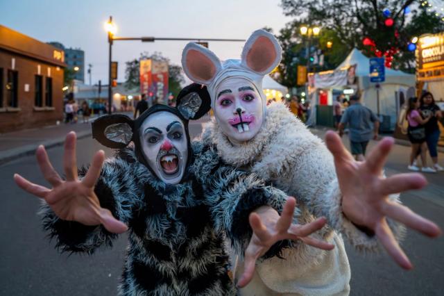 Two Fringe Artists on Festival Grounds dressed in giant rat costumes. Their arms reach out towards the camera, hands stretched wide!