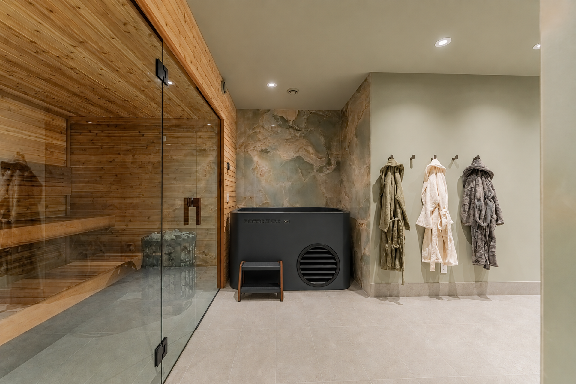 Home spa with glass-enclosed sauna, cold plunge tub and robes hanging on hooks.