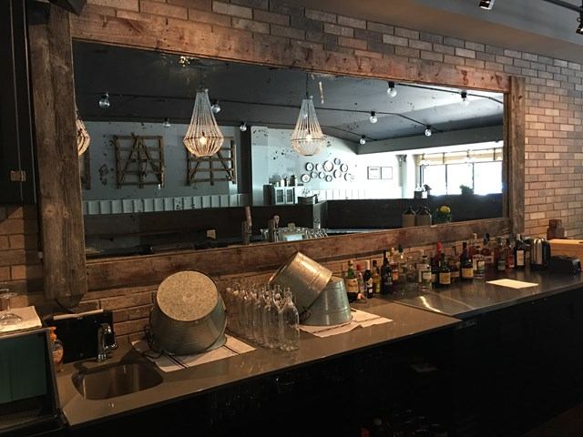 Bar counter with metal buckets, glassware and liquor bottles beneath a large wall mirror.