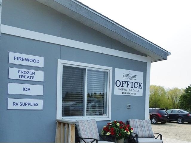 RV park office with signs for firewood, ice, and supplies, plus benches and flowers.